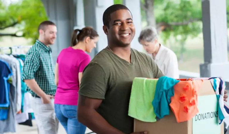 young man with a cardboard box full of clothes and some people at the backside