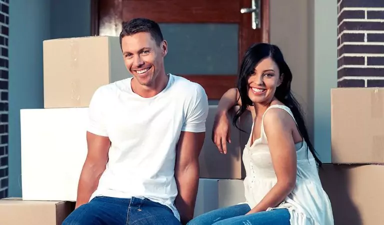 couple with some cardboard boxes sitting outside of a house
