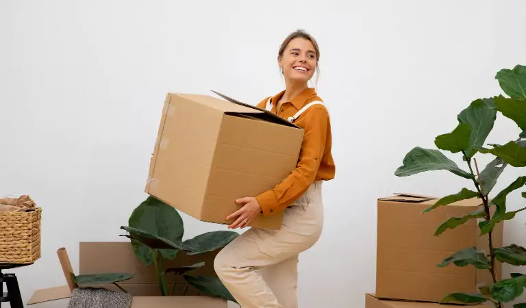 young woman looking happy inside of her new house and holding a cardboard box