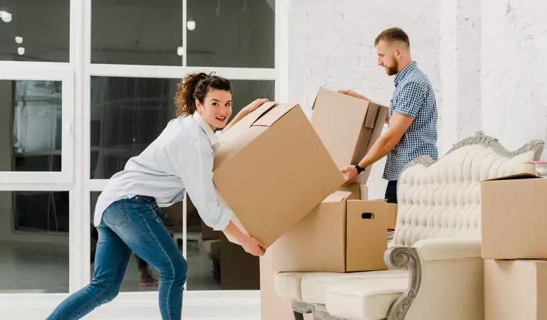 couple with a heavy cardboard box inside of a house