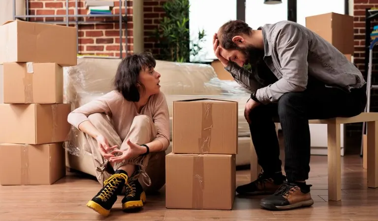Sad man sitting on a chair and a woman on the floor with moving boxes.