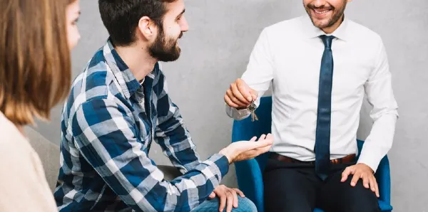 A person in white shirt giving key to another person in check shirt.