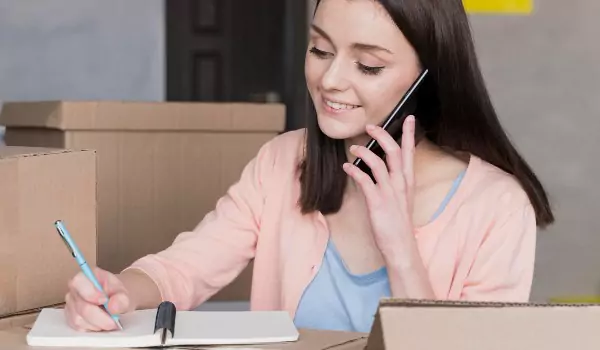 woman talking over a phone and noting down something