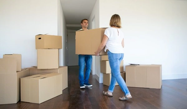 Married couple leaving apartment, carrying cartoon box to entrance together